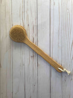 Eco-friendly body brush with a wooden handle and natural bristles, placed on a light wooden surface, ideal for dry brushing and exfoliation.