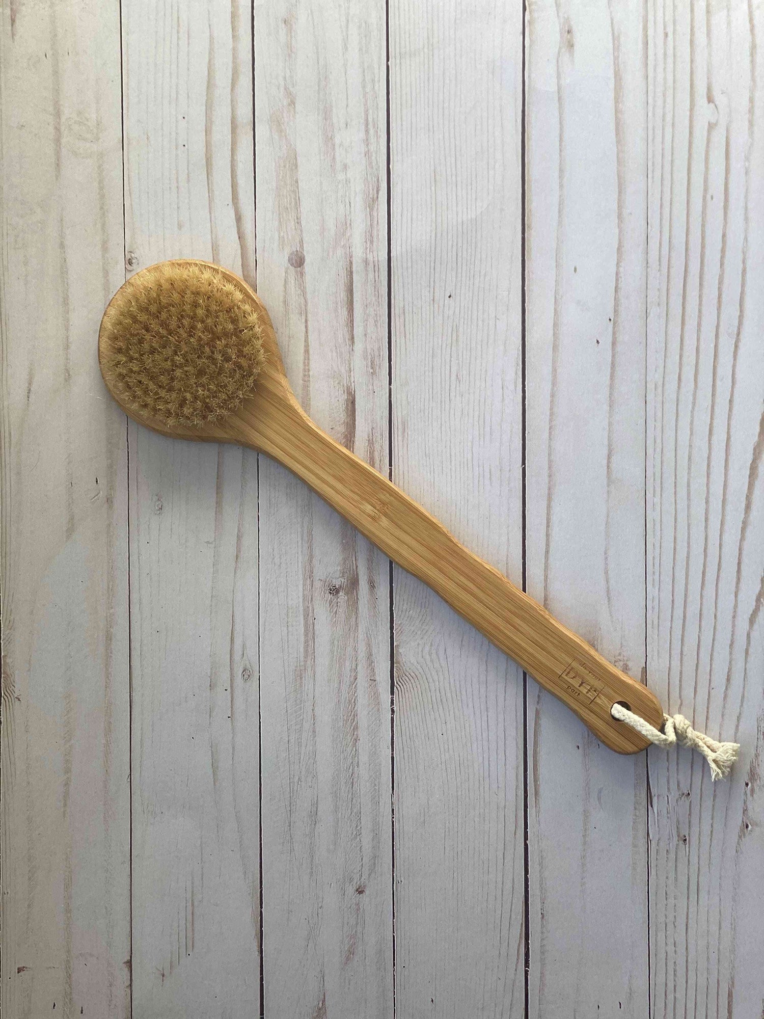 Eco-friendly body brush with a wooden handle and natural bristles, placed on a light wooden surface, ideal for dry brushing and exfoliation.