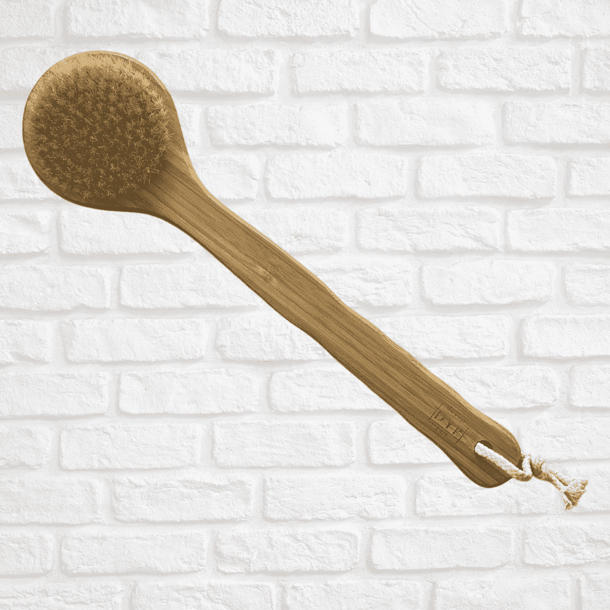 Eco-friendly body brush featuring a wooden handle and natural bristles, displayed against a white brick background, designed for dry brushing and skin care.