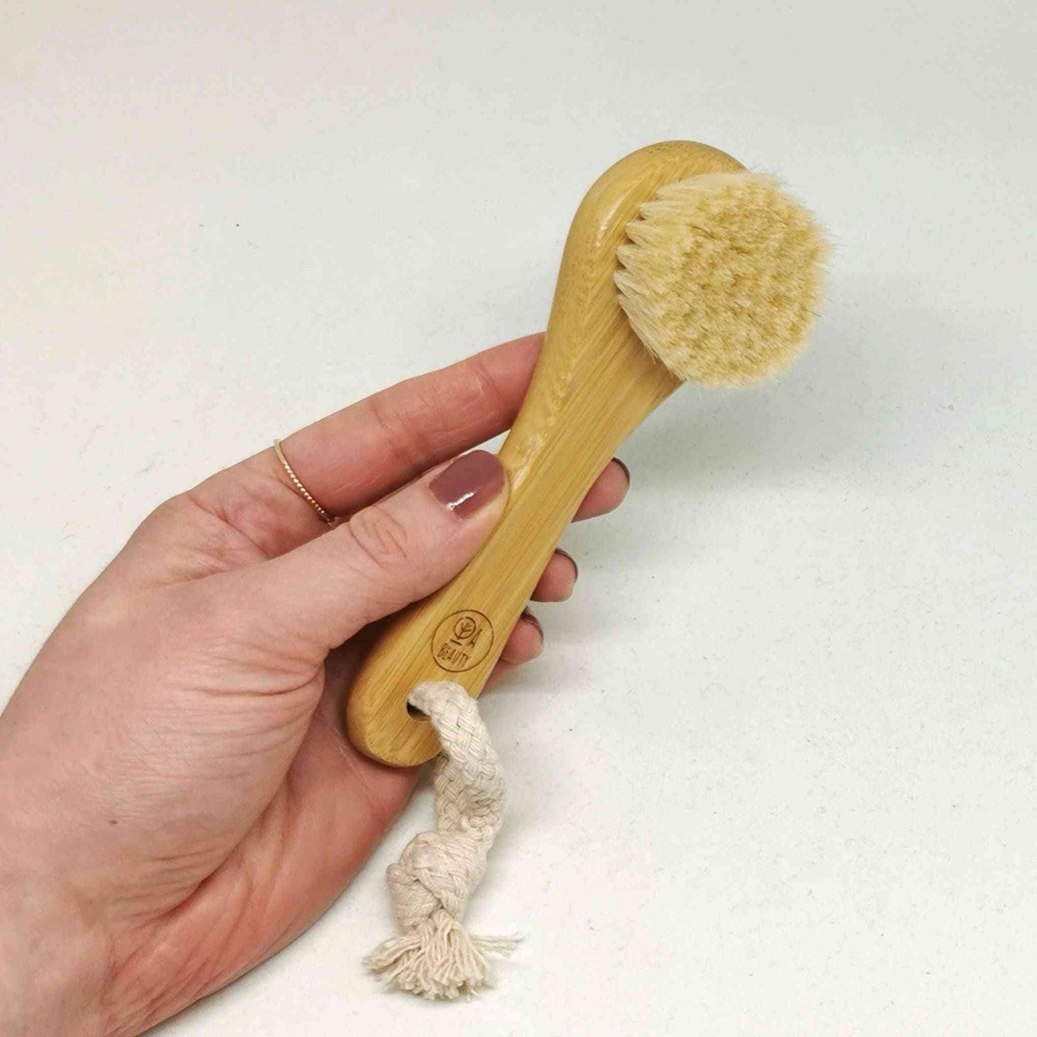 Hand holding the Soft Detox & Glow Face Brush with bamboo handle and soft goat bristles, showcasing its ergonomic design.