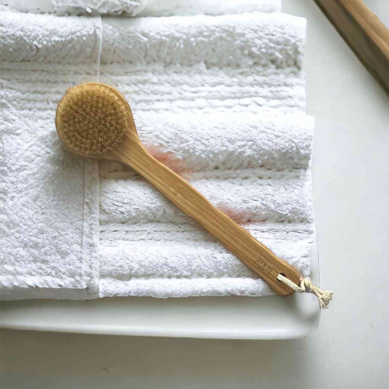 Eco-friendly body brush with natural bristles and a wooden handle, resting on white textured towels, perfect for skin exfoliation and lymphatic drainage.